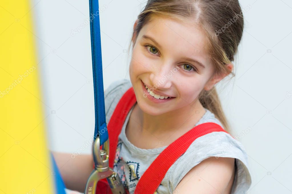 Active little girl in safety harness on climbing wall