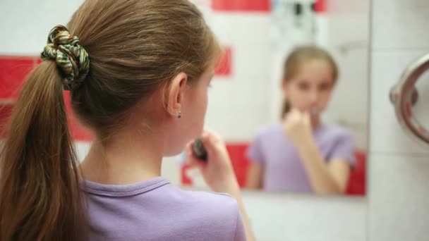 Zadní pohled na holčičku, kartáčky na zuby a při pohledu do zrcadla. Dívka čištění zubů v koupelně