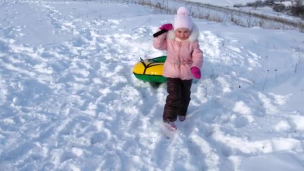 Маленька дівчинка гуляє по снігу, тягнучи з собою трубку — стокове відео