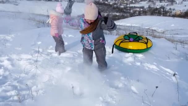 Två små systrar spelar i snön nära slangen — Stockvideo