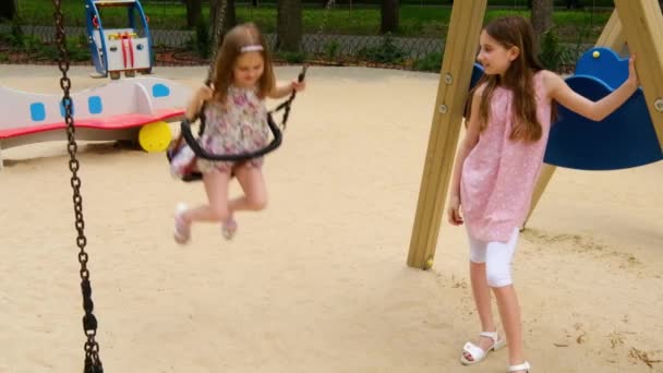 Маленькая девочка едет на качелях с сестрой — стоковое видео