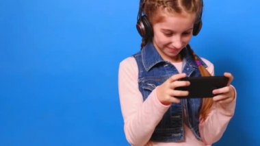 Küçük sevimli kız video oyun oynarken onun smartphone ve gülümseyen kulaklık