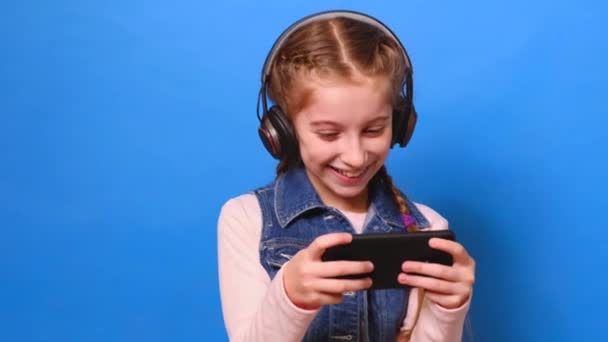 Молода дівчина в навушниках грає у відеогру на своєму смартфоні — стокове відео