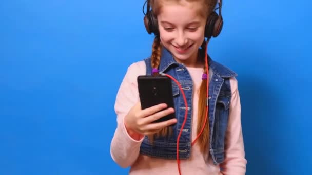 Little girl in headphones watching phone screen and smiling — Stock Video