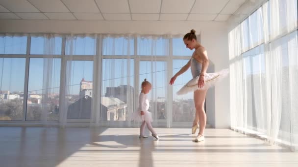 Молодая великолепная балерина учит дочь танцевать в студии — стоковое видео