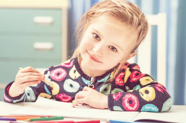 Çekici sarışın küçük kız kalemlerle çiziyor.