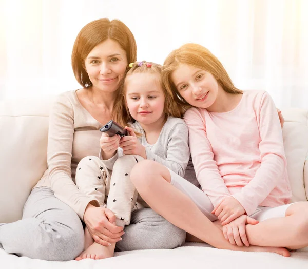 Mãe abraçando filhas enquanto assiste TV em casa — Fotografia de Stock