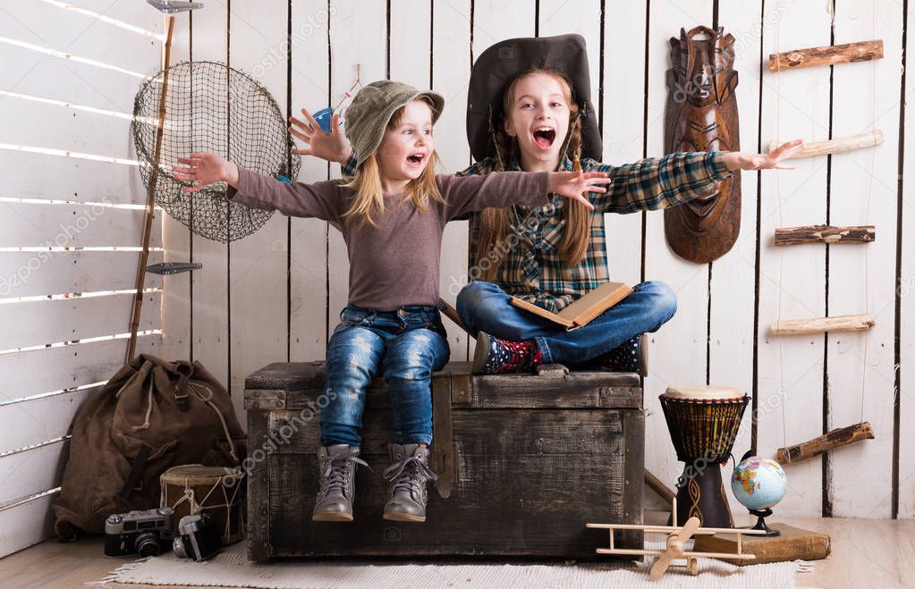 two little girls sitting on wooden chest with hands up 