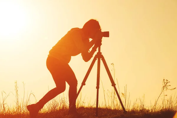 Silhueta de mulher fotógrafa fotografa paisagem de tiroteio ao pôr do sol — Fotografia de Stock