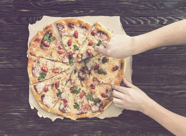 Hands cutting pizza top view on dark wooden background, toned wth instagram filter
