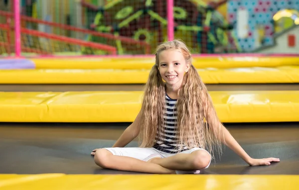 Little pretty smiling girl sitting on the trampoline — Stock Photo, Image