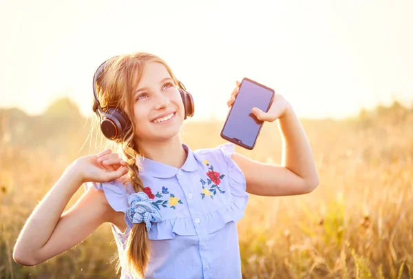 Ragazza sorridente tenere smartphone e ascoltare musica con le mani alzate — Foto Stock