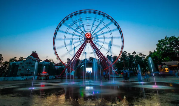 Vattenfontäner framför spinning Ferris flummig kvällen — Stockfoto