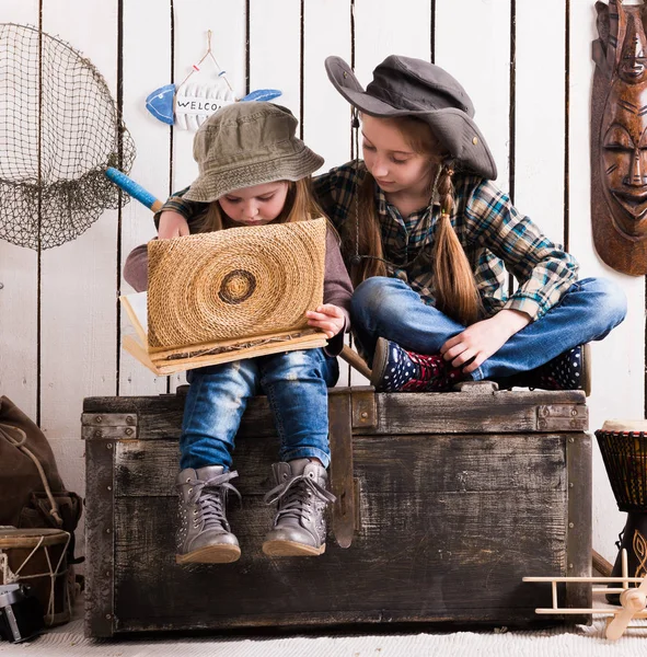 Dos lindas niñas en el pecho de madera viendo álbum —  Fotos de Stock