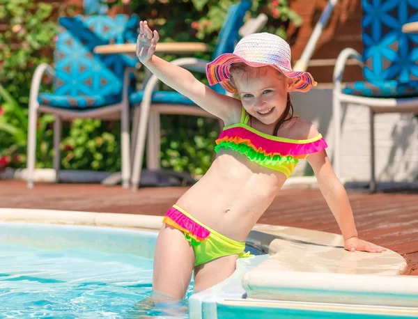 Little smiling blond girl in a bright swimsuit holding her hat — Stock Photo, Image