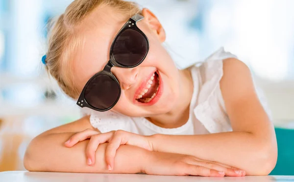 Pequeña chica rubia sonriente en gafas de sol negras — Foto de Stock