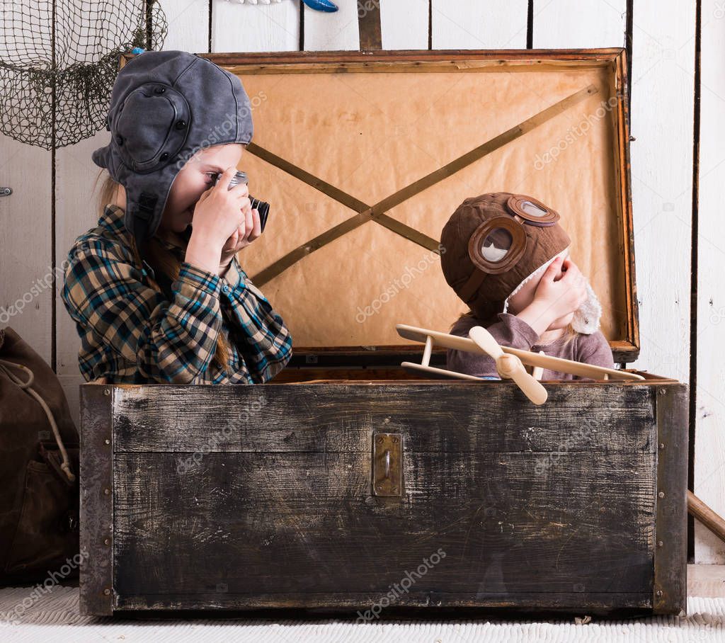 two little girls playing in big wooden chest with old camera