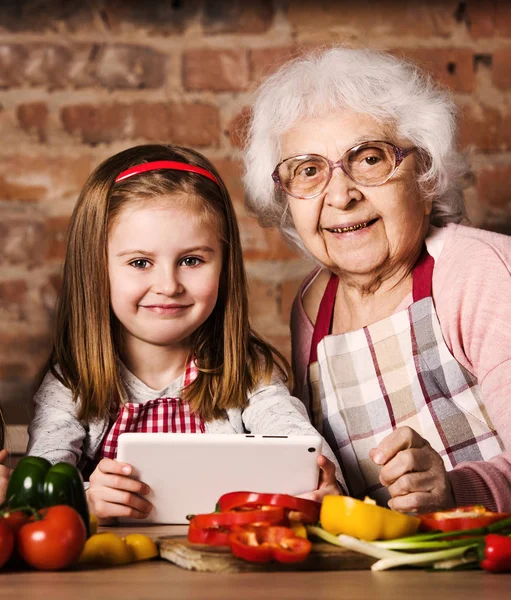 Vnučku a babička s tabletem v kuchyni — Stock fotografie