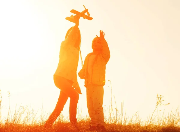 Silueta de dos hermanas jugando con el juguete del avión al atardecer — Foto de Stock