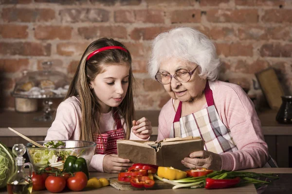 Babička s vnučkou pomocí vaření knihy — Stock fotografie