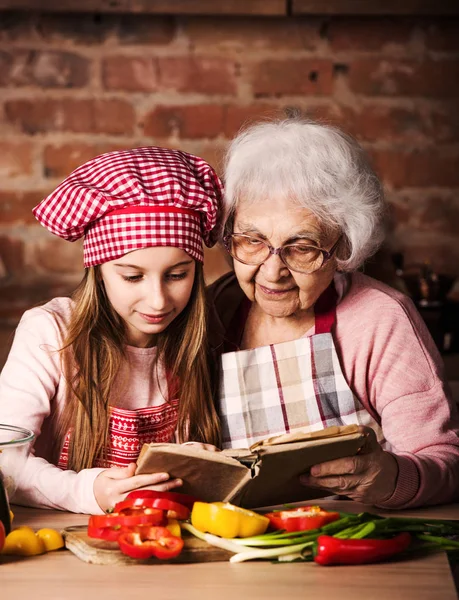 孙女阅读食谱书与奶奶 — 图库照片