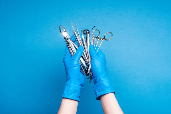 Mãos em luvas azuis segurando equipamentos odontológicos e instrumentos metálicos — Fotografia de Stock