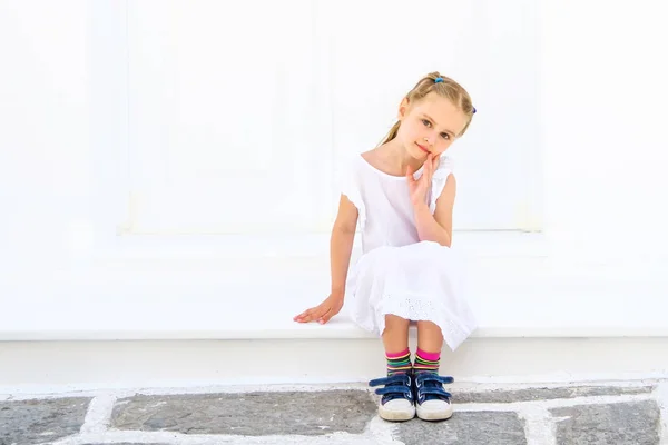 Little pretty blong girl in a white dress sitting outdoor — Stock Photo, Image