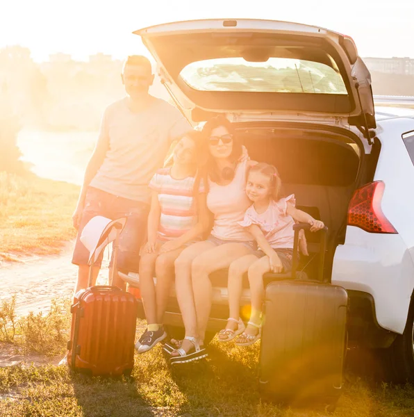 Happy family sitting on a trunk of a car with on a travel vacation