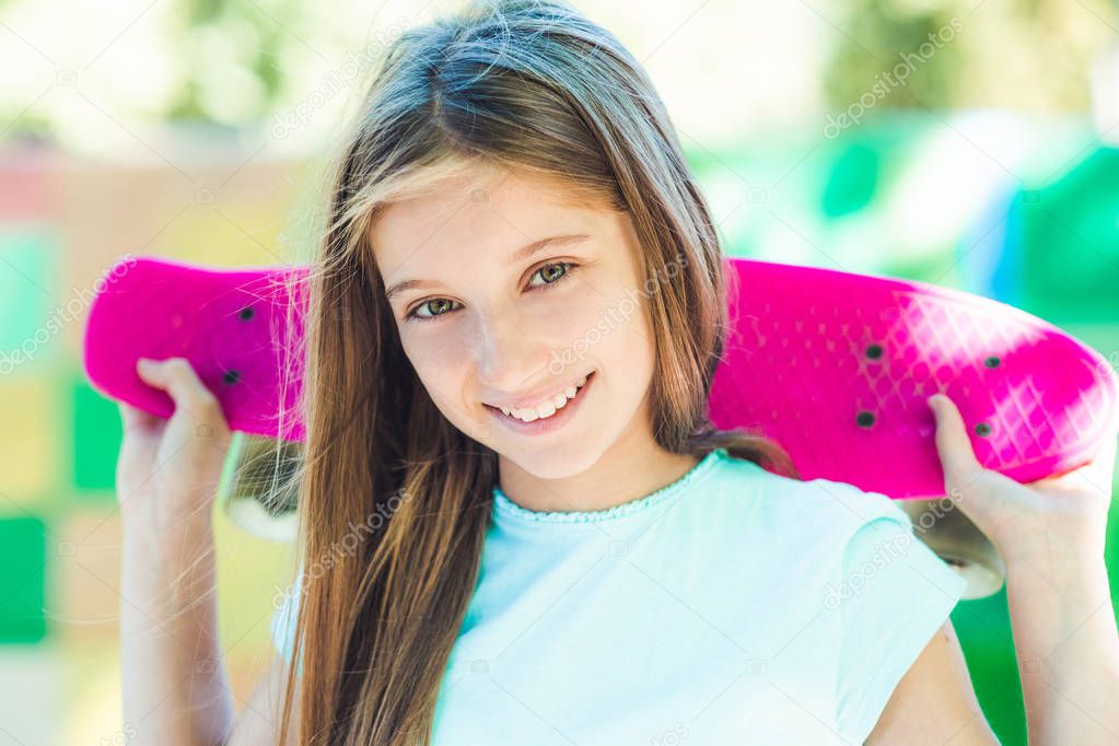 Smiling girl holding pink skateboard