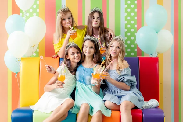 Meninas adolescentes muito sorridentes em vestidos e coroas sentar abraçando juntos no sofá colorido — Fotografia de Stock