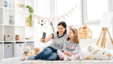 Gülümseyen anne ve kızı selfie çekiyorlar.