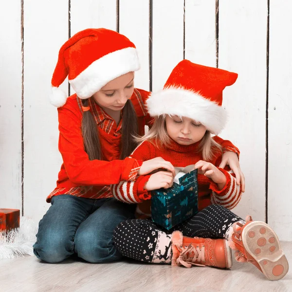 Två små flickor i röda hattar sitter på golvet med gåvor — Stockfoto