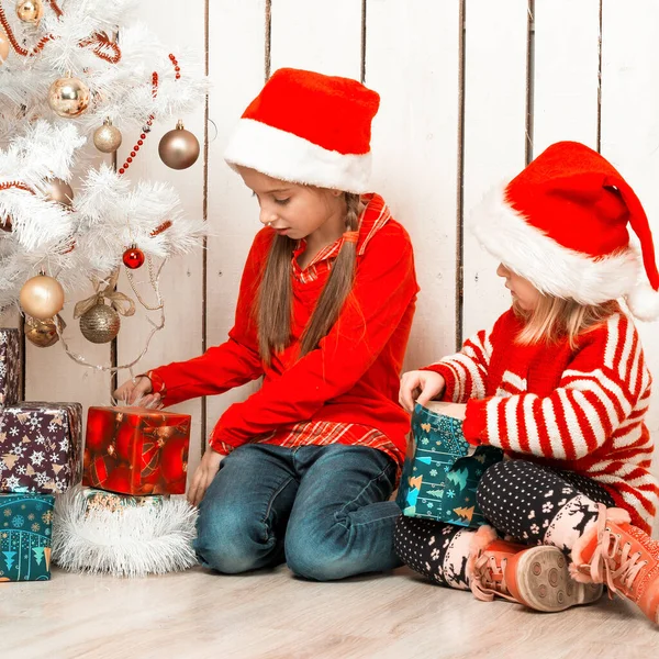 Két kislány kinyitja a karácsonyi ajándékokat a földön ülve. — Stock Fotó