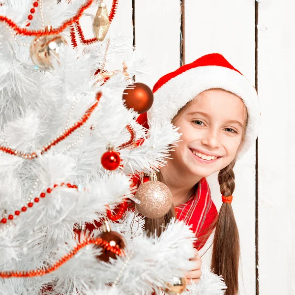 Sorrindo menina espreitando atrás de uma árvore de ano novo — Fotografia de Stock