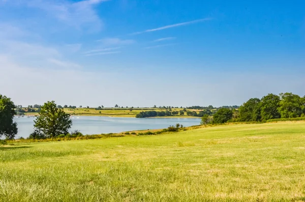 View across Rutland Water a large reservoir in Leicestershire with blue sky and grass. — ストック写真