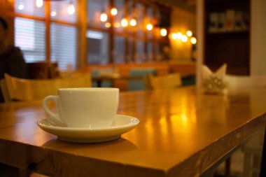 Lokantadaki ahşap bir masada bir fincan kahve duruyor. Kafenin arka planı bulanık. Sıcak akşam ışığı
