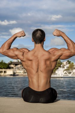 Çocuk kumsalda oturuyor, elleri havada.