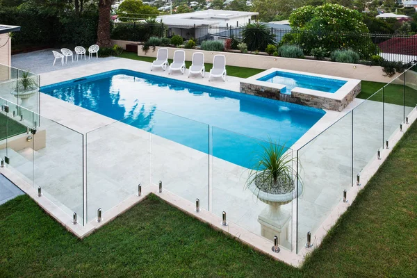Современный бассейн со стеклянными панелями рядом с газоном — стоковое фото
