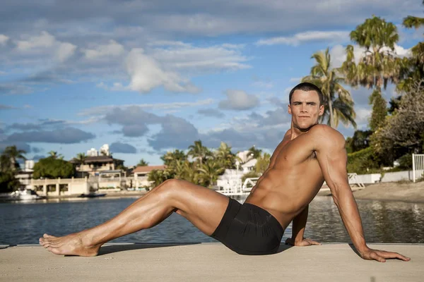 Genç bir çocuk kumsalda oturmuş gülümsüyor