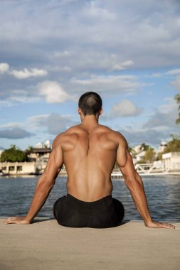 Güçlü adam düşünüyor ve sahilde oturuyor.