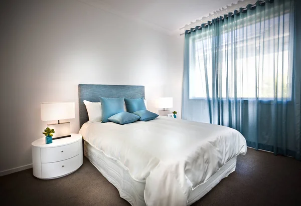 Современная кровать с белыми простынями и голубыми подушками — стоковое фото