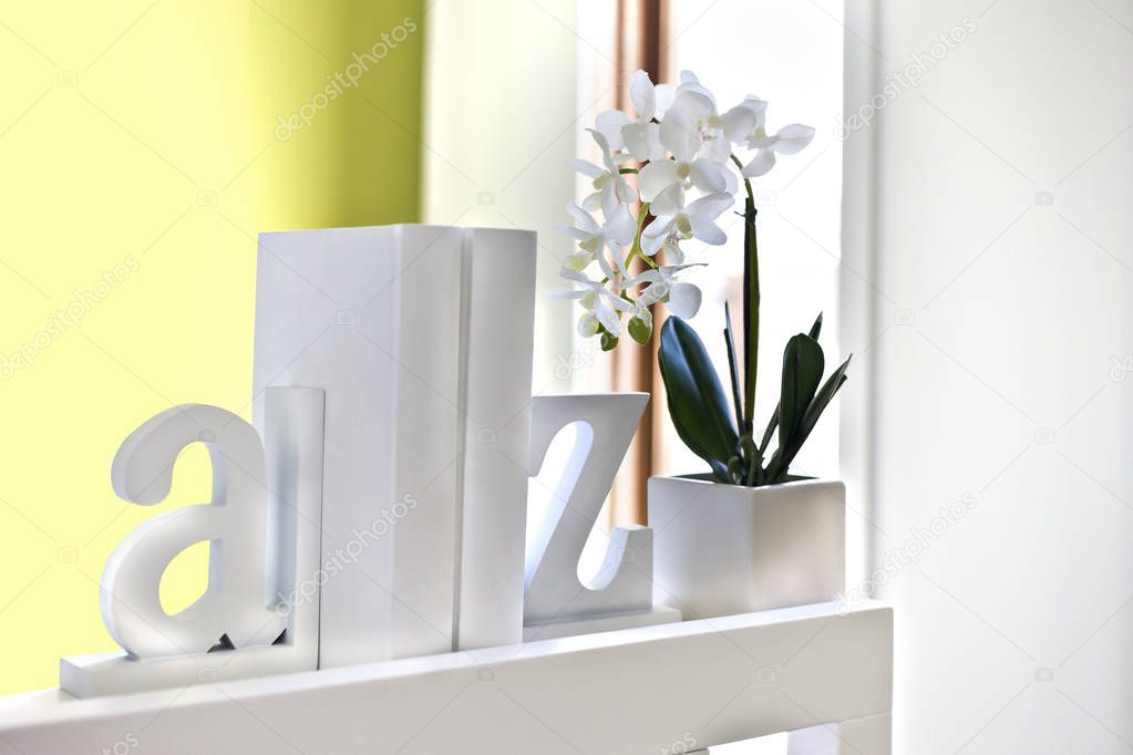 House interior decoration using 3d English letters and a white flowering plant, all letters and the supporter of the decor is white and made of wooden or cement, the background is blurred a little and probably near to the window