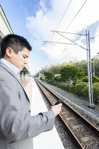 Smart man looking at mobile phone near station