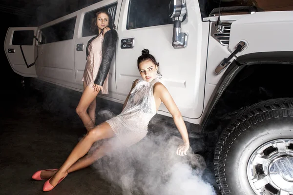 Two beauties posing in front of a high class vehicle