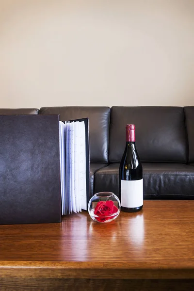 Бутылка вина с цветком розы и тяжелой книгой на столе — стоковое фото