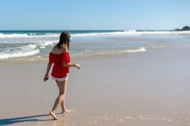 Genç ve çekici bir kız tropik cennet kumsalında yürüyor ve eğleniyor, Byron Bay, Avustralya