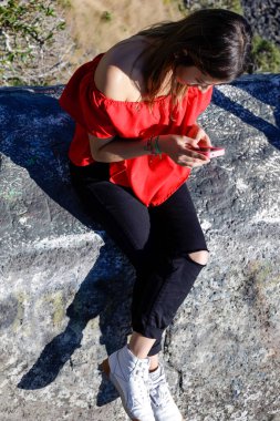 Yüksek açılı manzara, kıyı şeridinin üzerindeki kayada oturan ve manzaranın tadını çıkaran kırmızılı güzel bir kadın için.