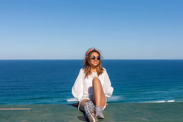 Fashionable caucasian girl enjoying the weekend at the beach. A cute young lady sitting near the ocean coast