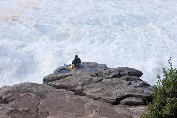 Osoba sedící na skále a sledující, jak bouřkové vlny narážejí do skal — Stock fotografie