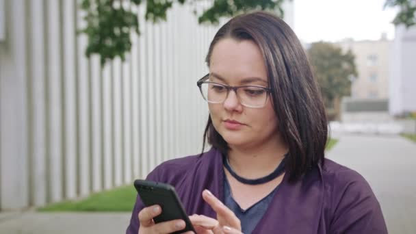 Joven dama usando gafas usando el teléfono en la ciudad — Vídeos de Stock